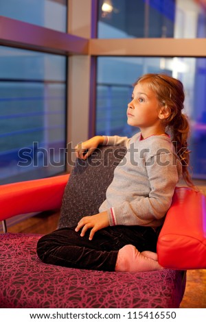Little girl sitting in chair in cabin with large windows in large cruise ship