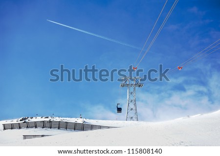 Funicular in alpine mountains on sunny winter day, jet plane on blue sky on background
