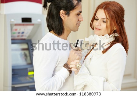 Dark-haired man with credit card in hand and red-haired woman stand face to face, she holds his hand and looks at card