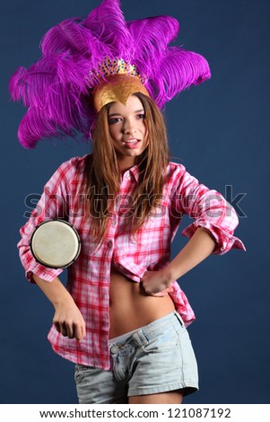 Singing girl in pink shirt in hat with feathers with small drum under her arm.