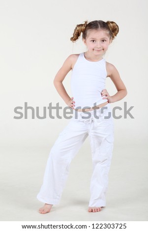 Little smiling girl in clean white clothes stands and poses.