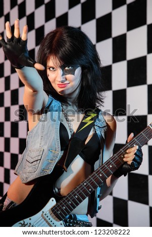 Young woman with electric guitar reaches out in studio with checkered background.