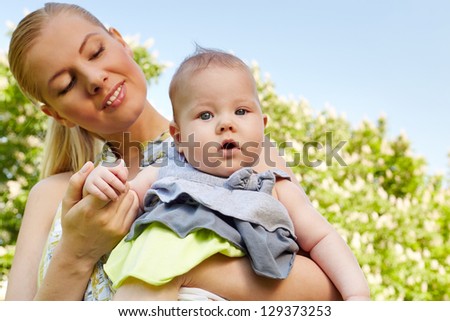 Young smiling mother holds her babygirl on her hands outdoors