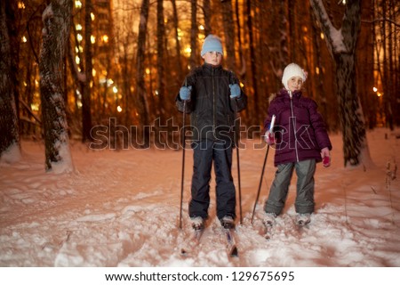 Girl and boy on ski at winter park in evening (some motion blur)