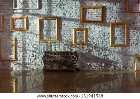 Empty picture frames on the brick wall and forged chest with candlesticks, side light.