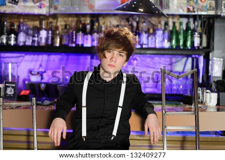 Glamorous boy in black shirt and white suspenders sits near bar counter.