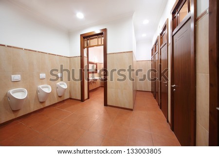 Light and clean public toilet with urinals, red tiles and wooden doors.
