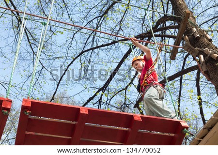Young climber going to go on a suspension bridge on high ropes course.
