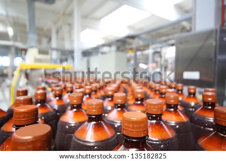 Many brown plastic bottles with beer and cap at big modern brewery.