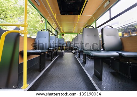Rows of grey seats inside clear saloon of empty city bus with skylight.