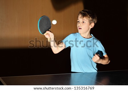 little boy wearing blue shirt playing ping pong; concentrated face