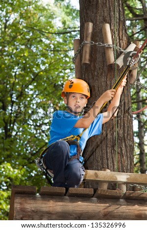 Young boy with equipment climber ready to go down from the tree.