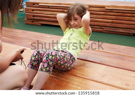 Little girl makes abdominal crunches for limited time on wooden platform