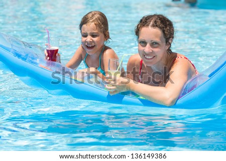 Happy mother and daughter swimming in the pool on an inflatable mattress with a drink in hand