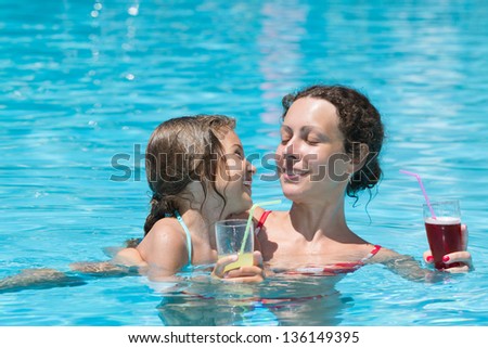 Mother and daughter swimming in the pool with a drink in hand
