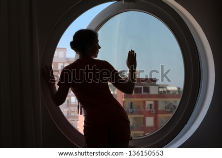 The dark silhouette of a beautiful woman on the background of the round window with blue sky.