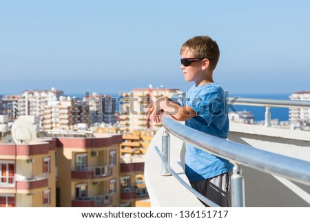A boy stands on the balcony of the hotel and looks into the distance on the background of the cityscape and skyline