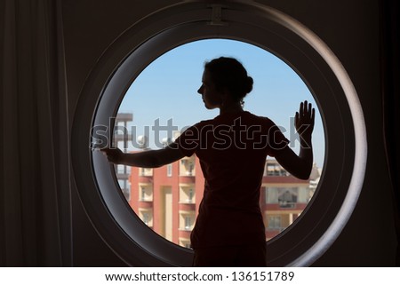 The dark silhouette of a beautiful woman on the background of the closed round window with blue sky.
