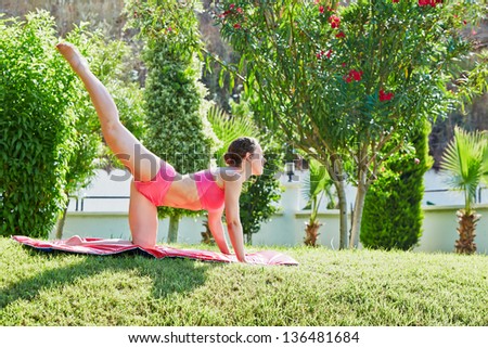 Young woman does leg swing on matting in morning garden
