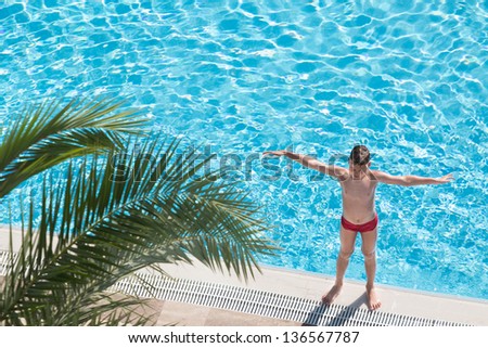 Boy sunbathe on the edge of the pool near palm leaf and raised his hands