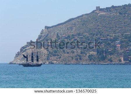 Pirate ship with black sails floats past beautiful landscape of the ancient wall