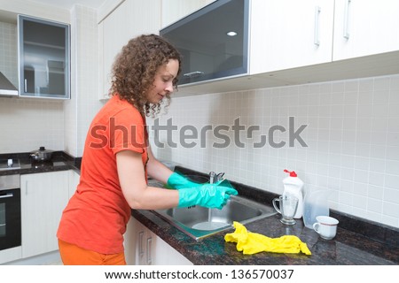 Cute housewife washing dishes with a sponge in rubber gloves