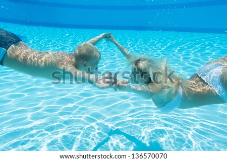Mother and son swim underwater holding hands in the pool