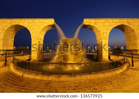 Fountain in the form of two waterfalls in the night sky behind the beach and the sea