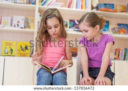 Two little girls are concentrated in the library reading a book, focus on left girl