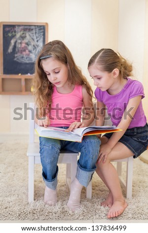 Two girls are sitting in the game room on the chairs and read a book