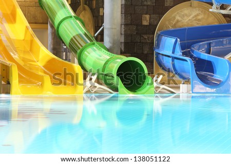 Big multi-colored water slides and pool in indoor aquapark. Yellow, green and blue slides.