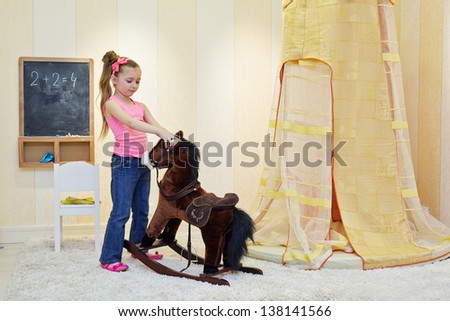 Little girl plays with hobbyhorse in play room