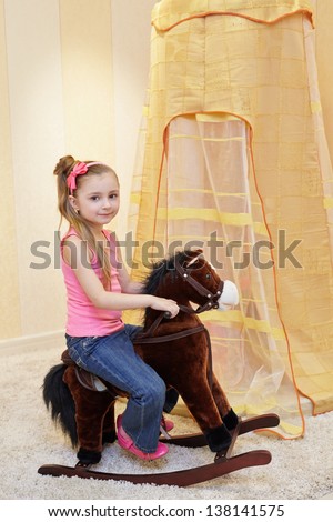 Little girl rocks on rocking horse in play room