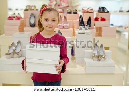 Little girl stands and holds two shoe boxes in shoe store