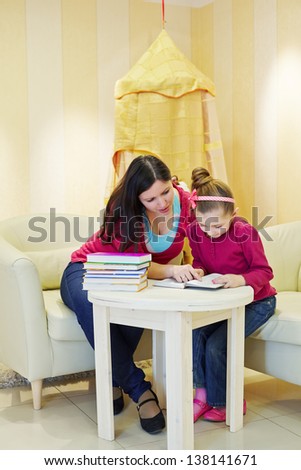 Mother and daughter read book, sitting at table in playroom