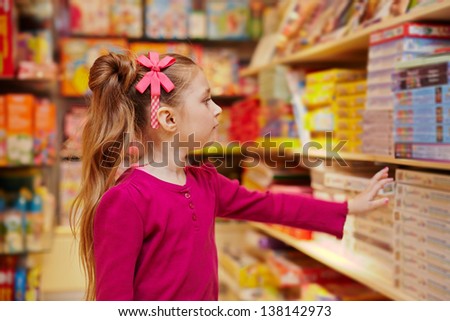 Little girl stretches to shelf with table games in book department of store