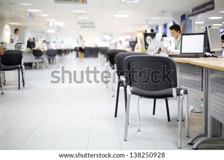 Men And Women Work At Computers In Car Dealership Office. Shallow Depth Of Field. Focus On Nearest Chair.