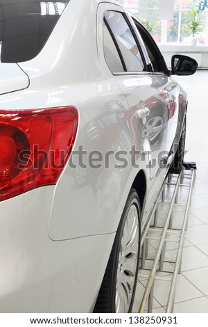 Back red lights of new white shining car standing in office of shop selling cars.