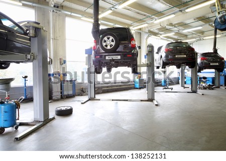 Four Black Cars On Lifts In Small Service Station. Cars Prepared To Diagnosis And Repair.