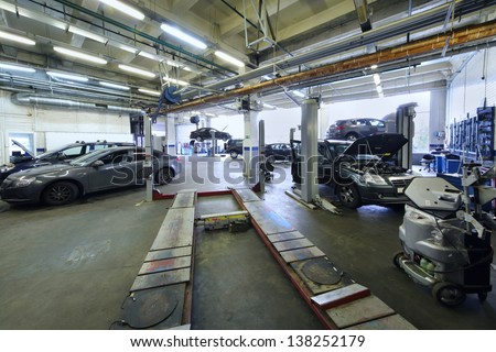 Many cars stand in car garage with special equipment for repair.