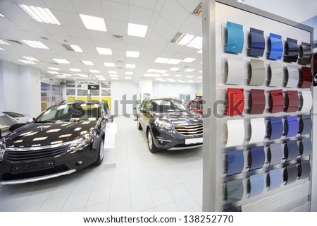 New black cars stand in car shop near stand with samples of paint for body. Focus on stand with samples.