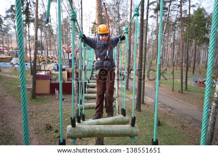 Boy climber walks on the rope bridge on ropes course