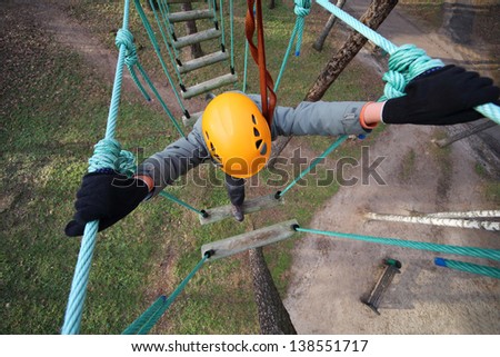 Boy climber walks on the rope bridge, the view from above