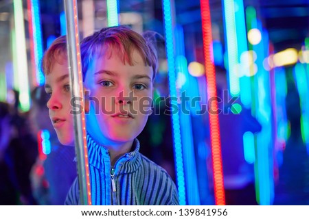 Boy stands in mirror labyrinth illuminated with color lights