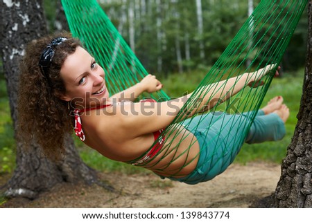Young smiling barefooted woman swings in hammock, head turned back