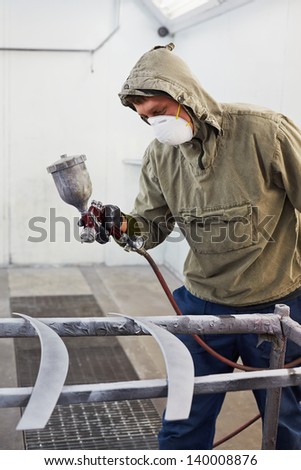Man in protective clothes and respirator paints car details in paint-spraying booth