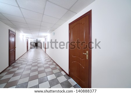 Long bright hallway with wooden doors and floor covered with tiles.