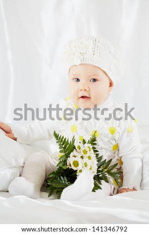 Portrait of little girl in white clothes on white coverlet with bunch of flowers
