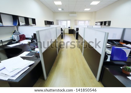 Empty places of work separated by partition with desktops and papers.