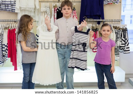 The boy helps cute girls to choose dress in shop of childrens clothing